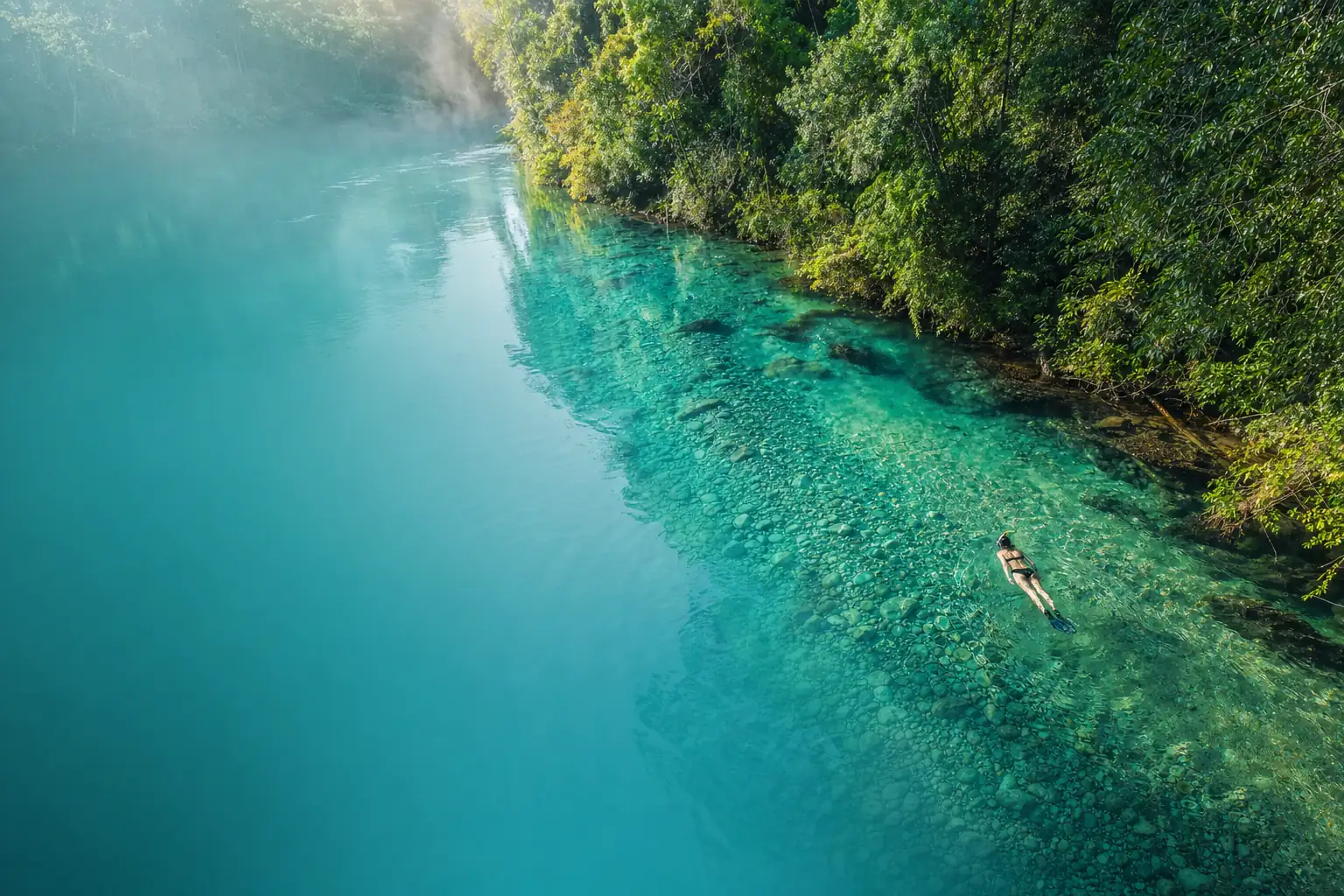 Vista aérea de um rio de água turquesa transparente cortando a floresta, com um flutuador na superfície